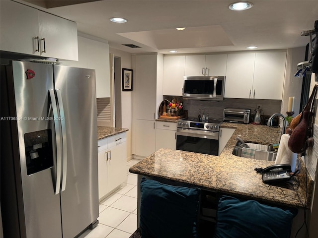 kitchen with sink, stainless steel appliances, tasteful backsplash, a tray ceiling, and kitchen peninsula