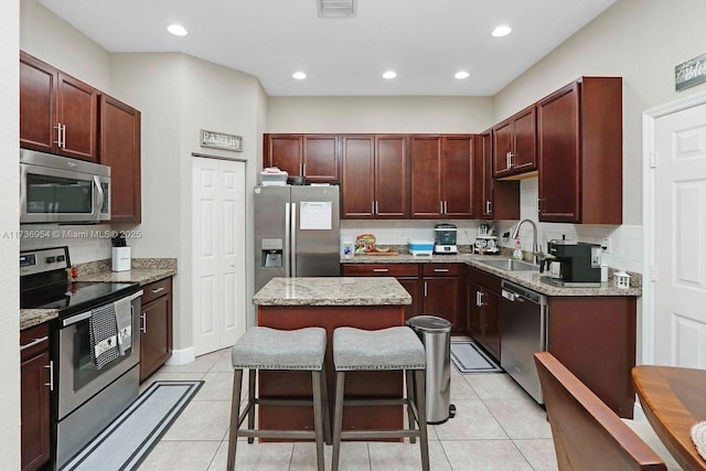 kitchen featuring light tile patterned flooring, a kitchen island, a breakfast bar, sink, and stainless steel appliances