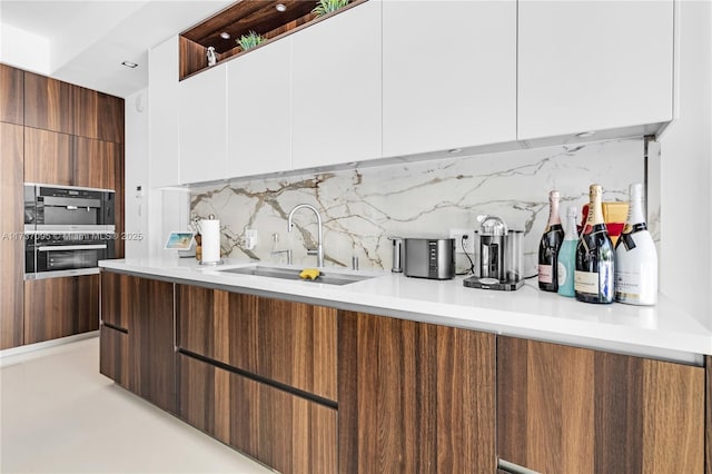 kitchen with white cabinetry, double wall oven, sink, and tasteful backsplash