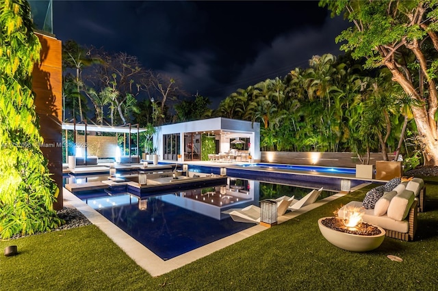 pool at twilight featuring an outdoor structure, a fire pit, and a lawn