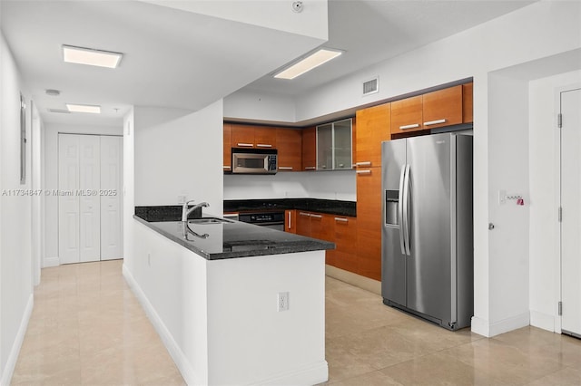 kitchen with appliances with stainless steel finishes, sink, dark stone countertops, light tile patterned floors, and kitchen peninsula