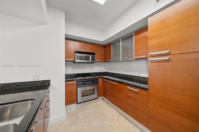 kitchen featuring sink, light tile patterned floors, dark stone counters, and appliances with stainless steel finishes