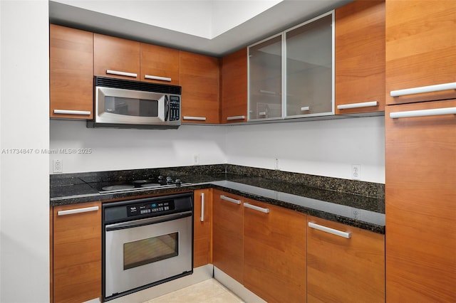 kitchen with light tile patterned flooring, appliances with stainless steel finishes, and dark stone countertops