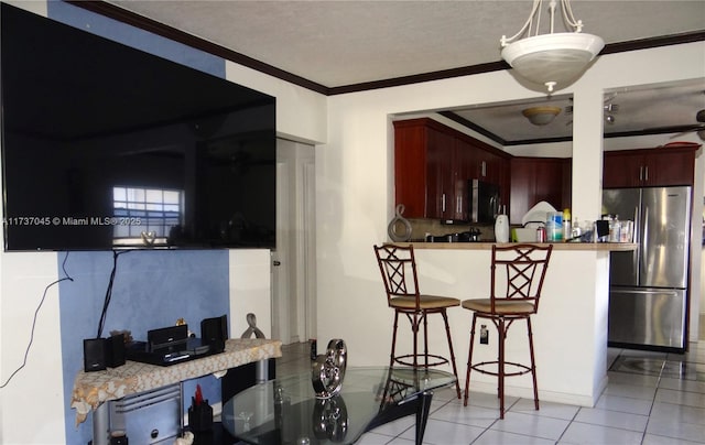 kitchen featuring a breakfast bar, decorative light fixtures, light tile patterned floors, stainless steel appliances, and crown molding