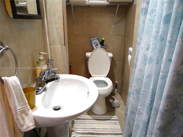 bathroom with toilet, curtained shower, sink, and tile walls