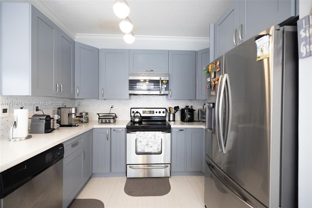 kitchen with appliances with stainless steel finishes, gray cabinetry, light tile patterned floors, and decorative backsplash