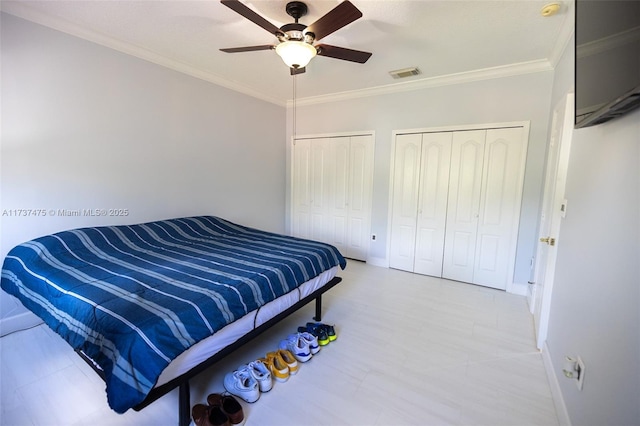 bedroom with crown molding, ceiling fan, and two closets