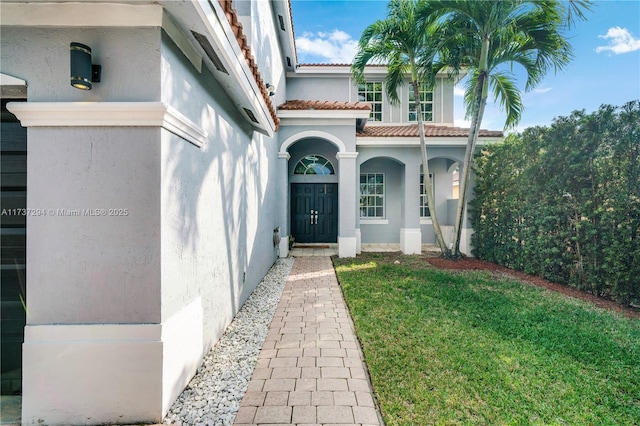 view of exterior entry featuring a yard, a tile roof, and stucco siding