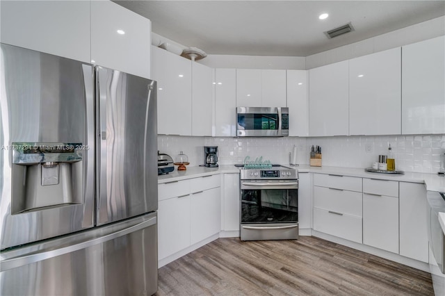 kitchen featuring backsplash, light wood-type flooring, white cabinets, and appliances with stainless steel finishes