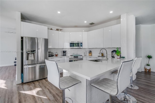 kitchen with appliances with stainless steel finishes, a breakfast bar, wood finished floors, a peninsula, and a sink