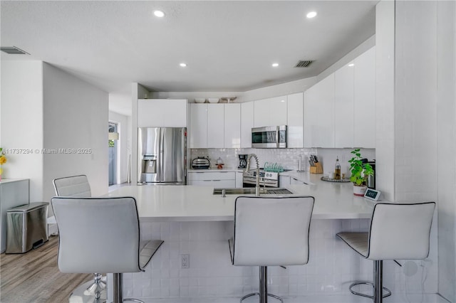 kitchen with white cabinetry, tasteful backsplash, a kitchen breakfast bar, kitchen peninsula, and stainless steel appliances