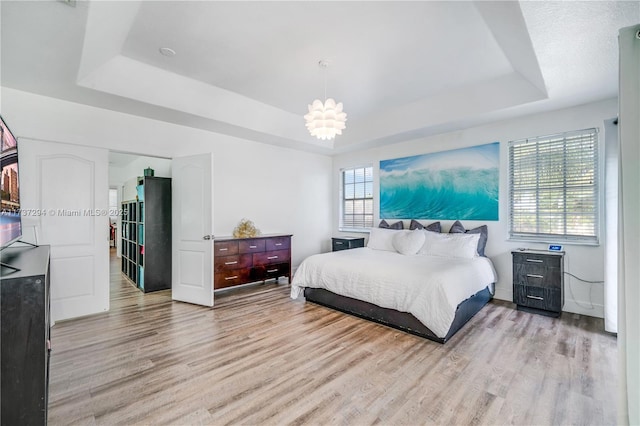 bedroom with a chandelier, light hardwood / wood-style floors, and a tray ceiling