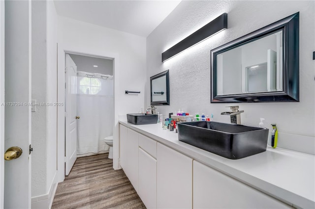 full bath featuring toilet, wood finished floors, a sink, a shower, and double vanity