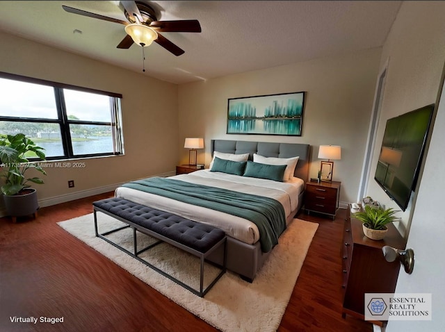 bedroom featuring dark wood-type flooring, ceiling fan, and a water view