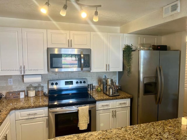 kitchen with stainless steel appliances, white cabinets, dark stone counters, and decorative backsplash