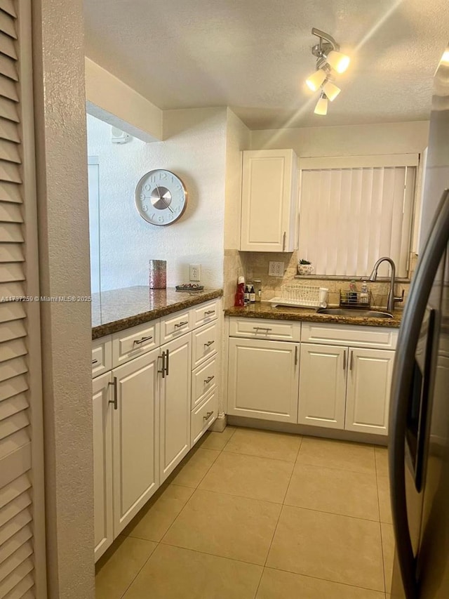 kitchen featuring white cabinetry, sink, light tile patterned floors, and dark stone counters