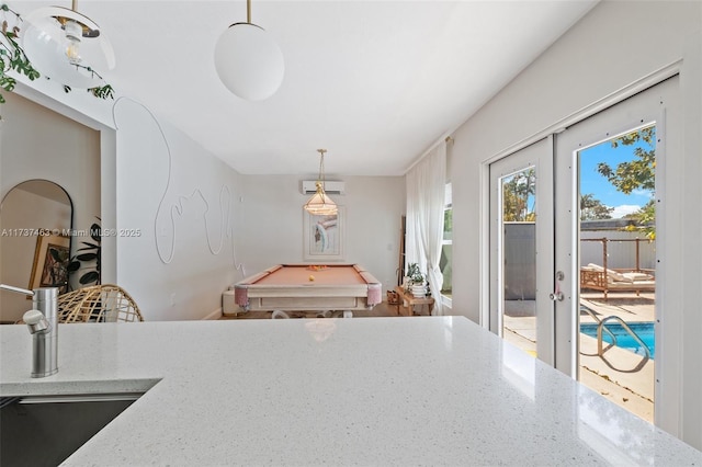 kitchen with sink, hanging light fixtures, light stone counters, a wall unit AC, and french doors