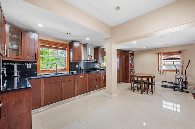 kitchen featuring dark countertops, stacked washer / dryer, wall chimney exhaust hood, and a sink