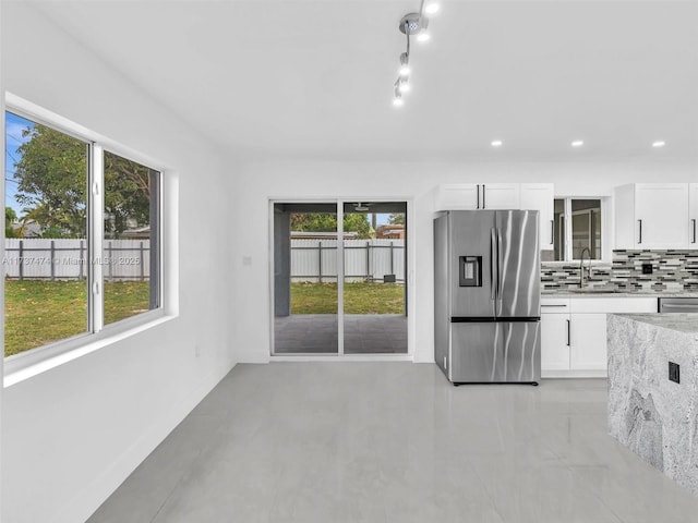 kitchen with white cabinets, a sink, light stone countertops, tasteful backsplash, and stainless steel refrigerator with ice dispenser