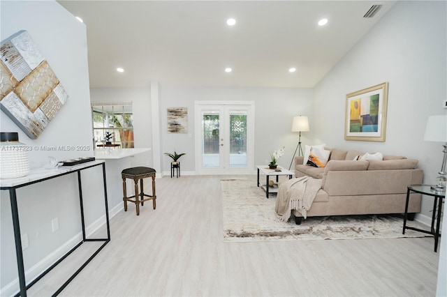 living room with french doors, plenty of natural light, vaulted ceiling, and light hardwood / wood-style floors