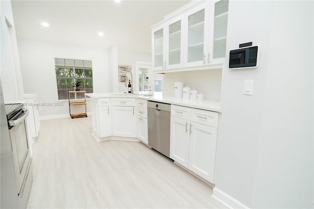 kitchen with sink, white cabinetry, light hardwood / wood-style flooring, kitchen peninsula, and stainless steel appliances