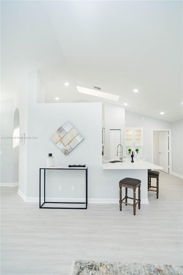 interior space with lofted ceiling, sink, a breakfast bar, and light wood-type flooring