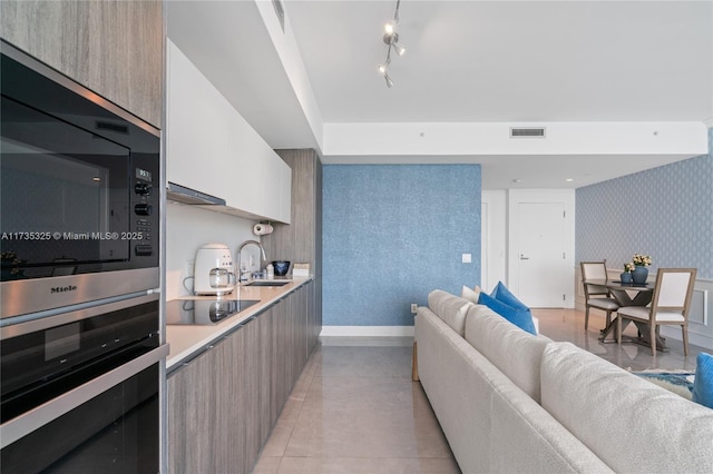 kitchen featuring built in microwave, rail lighting, sink, white cabinetry, and black electric stovetop