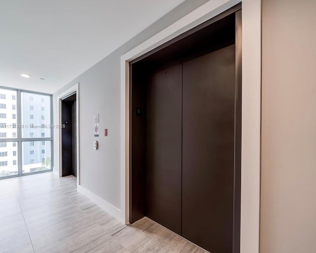 hallway with elevator, a wall of windows, and light hardwood / wood-style flooring