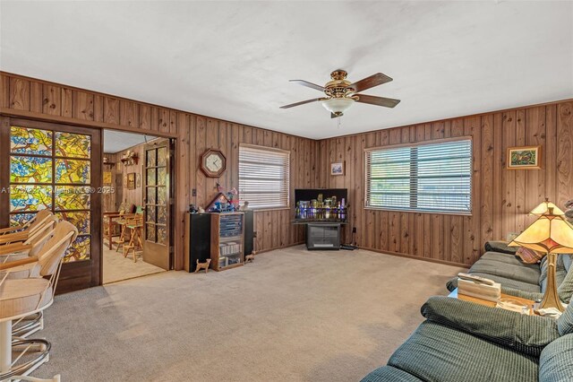 living room featuring a wealth of natural light, light colored carpet, ceiling fan, and wood walls