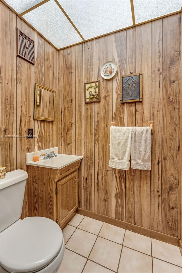 bathroom featuring tile patterned flooring, vanity, wooden walls, and toilet