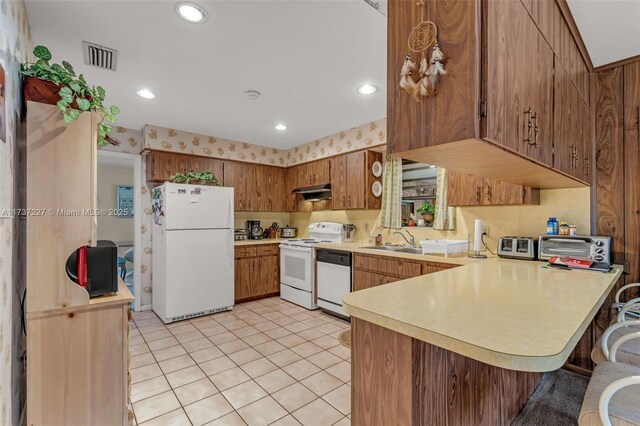 kitchen featuring sink, white appliances, light tile patterned floors, a kitchen breakfast bar, and kitchen peninsula