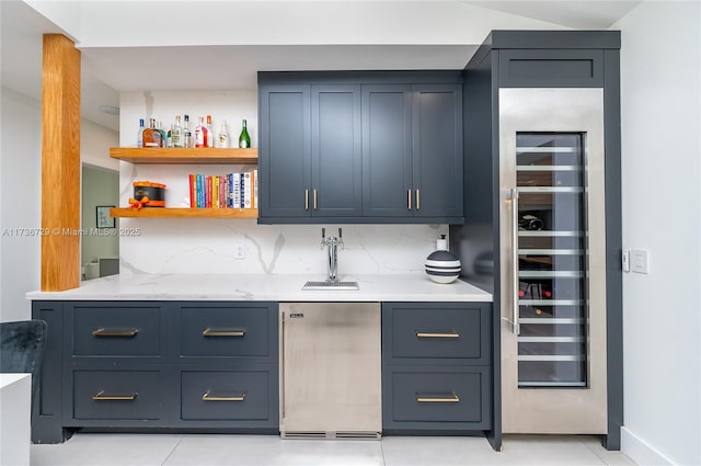 bar featuring blue cabinetry, light stone counters, luxury fridge, decorative backsplash, and beverage cooler