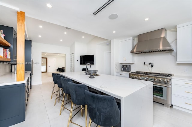 kitchen featuring white cabinetry, stainless steel range, wall chimney exhaust hood, and a center island with sink