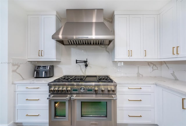 kitchen featuring white cabinetry, wall chimney range hood, light stone counters, and double oven range