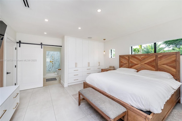 bedroom with light tile patterned flooring, a barn door, and ensuite bathroom