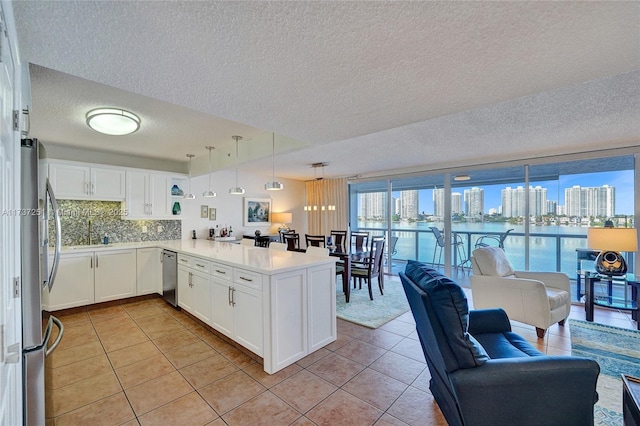 kitchen featuring light tile patterned floors, appliances with stainless steel finishes, white cabinetry, decorative light fixtures, and kitchen peninsula