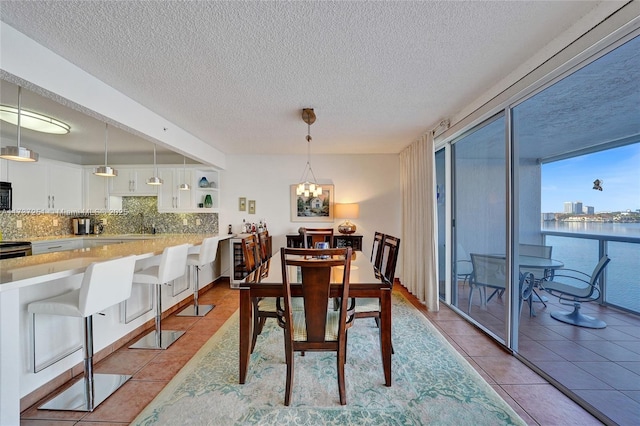 dining room featuring a textured ceiling, light tile patterned flooring, a chandelier, and a water view