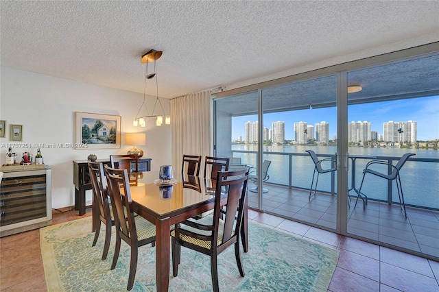 dining space featuring wine cooler, tile patterned flooring, a textured ceiling, and a water view