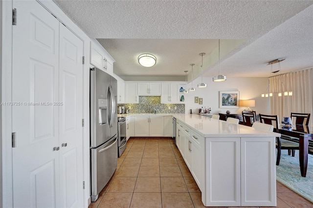 kitchen with light tile patterned floors, hanging light fixtures, stainless steel appliances, white cabinets, and kitchen peninsula