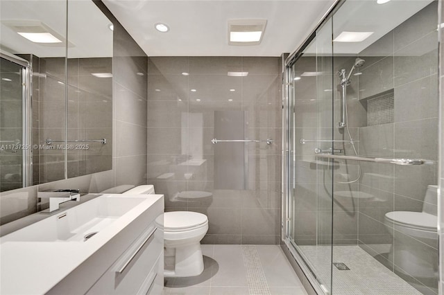 bathroom with walk in shower, toilet, tile walls, vanity, and tile patterned flooring