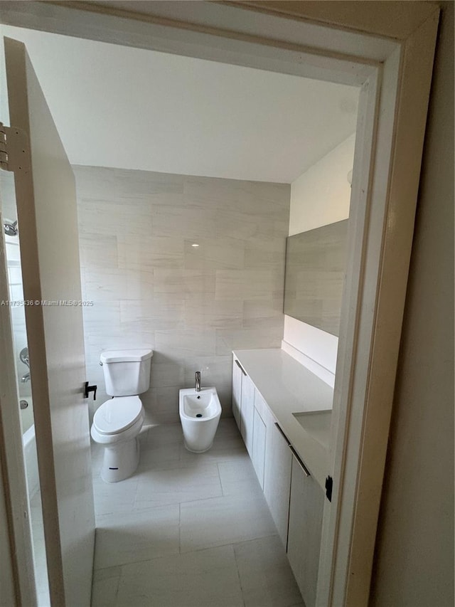 bathroom with tile walls, vanity, toilet, a bidet, and tile patterned floors