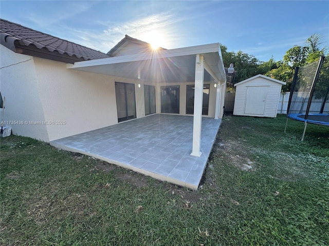 back of property with a storage unit, a yard, a trampoline, and a patio area