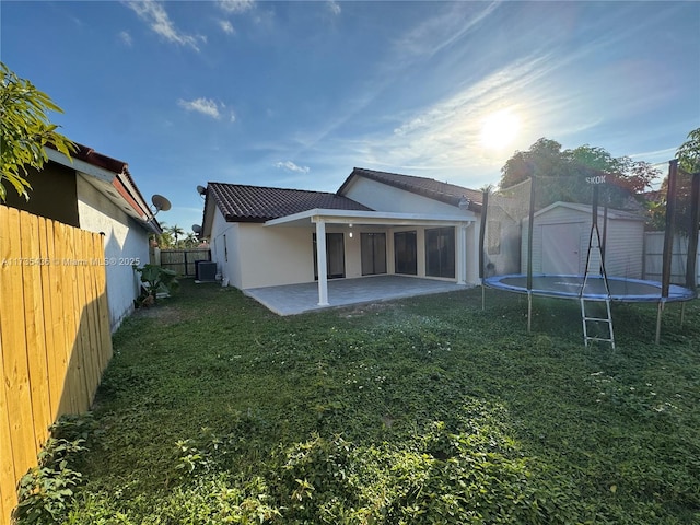 back of house with a patio, a yard, cooling unit, and a trampoline