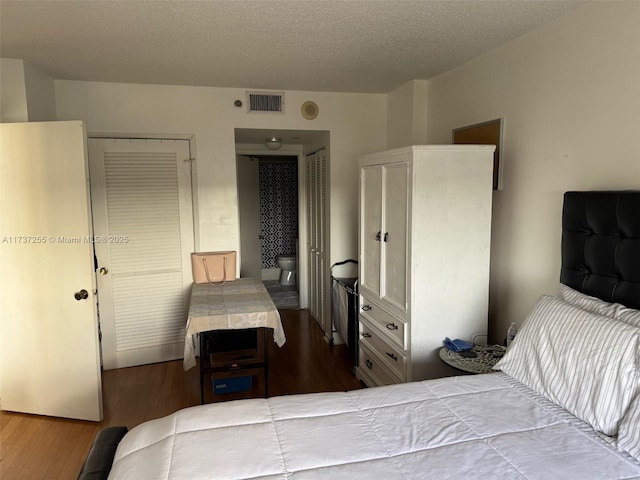 bedroom with ensuite bathroom, dark wood-type flooring, and a textured ceiling