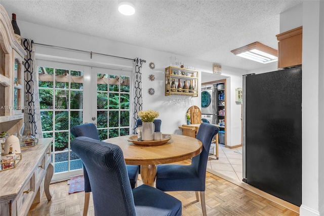 dining area with french doors, light parquet flooring, stacked washer / dryer, and a textured ceiling