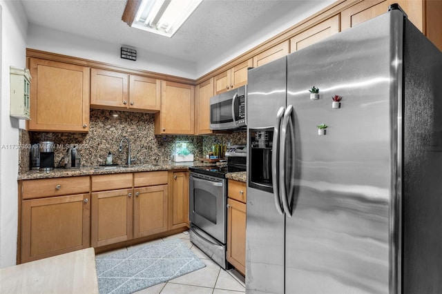 kitchen featuring appliances with stainless steel finishes, stone countertops, sink, backsplash, and light tile patterned floors