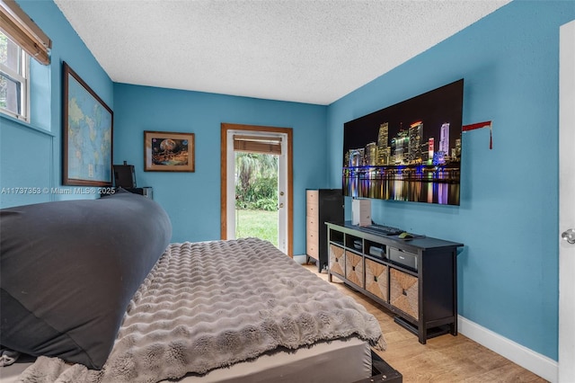 bedroom featuring access to exterior, a textured ceiling, and light hardwood / wood-style flooring