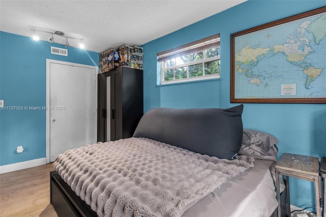 bedroom featuring a closet, light hardwood / wood-style flooring, rail lighting, and a textured ceiling