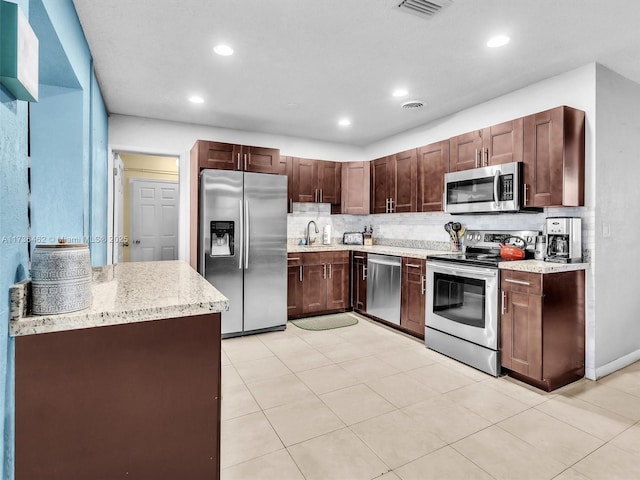 kitchen featuring sink, decorative backsplash, dark brown cabinetry, light stone counters, and stainless steel appliances