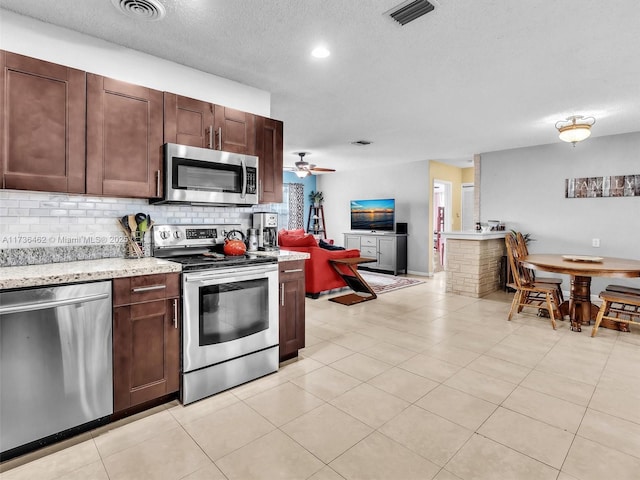 kitchen with appliances with stainless steel finishes, decorative backsplash, ceiling fan, light stone countertops, and a textured ceiling